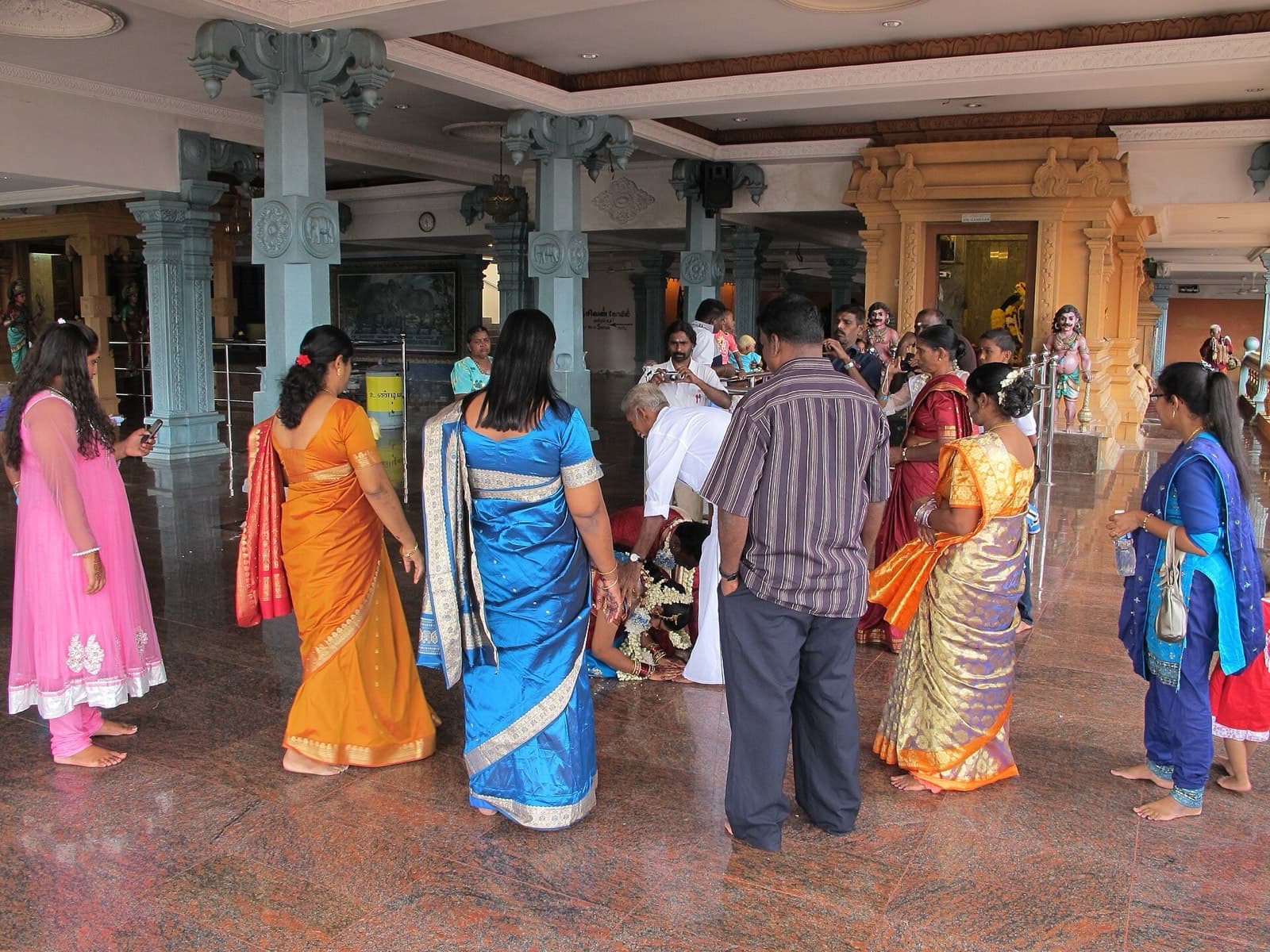 Family and guests in silk sarees gather around a couple during a ritual at a Hindu temple in Malaysia