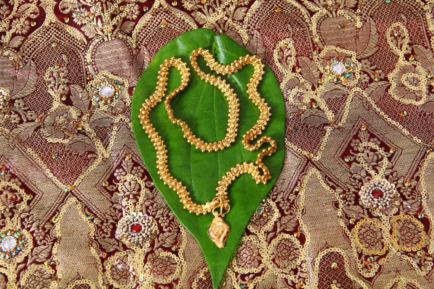 A gold thali chain and pendant resting on a betel leaf over red and gold silk