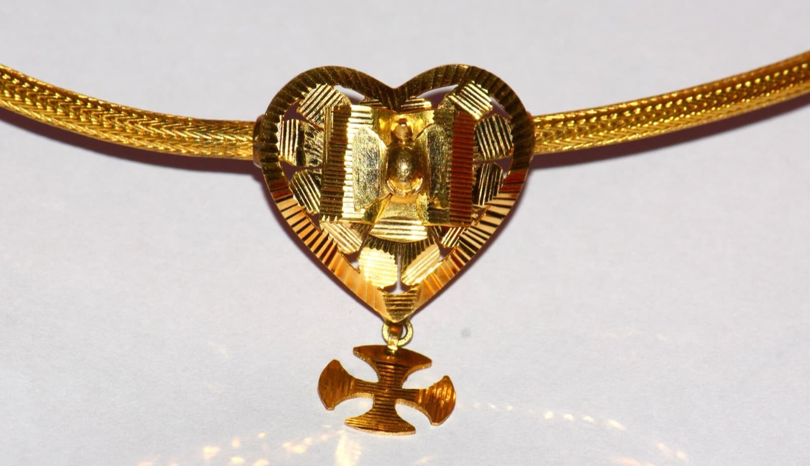 A gold Christian thali with a heart-shaped pendant and a small cross